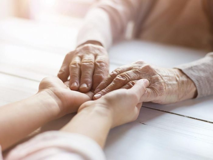 Mains d'une personne âgée tenues par des mains plus jeunes, massage et lien social contre l'isolement